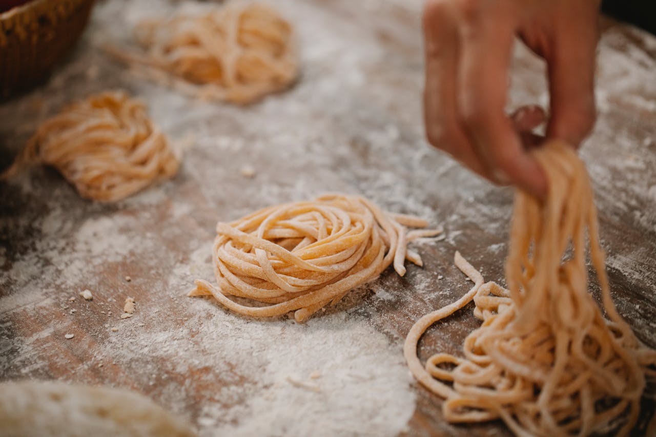 From above crop anonymous chef forming raw pasta nests on table covered with flour in kitchen